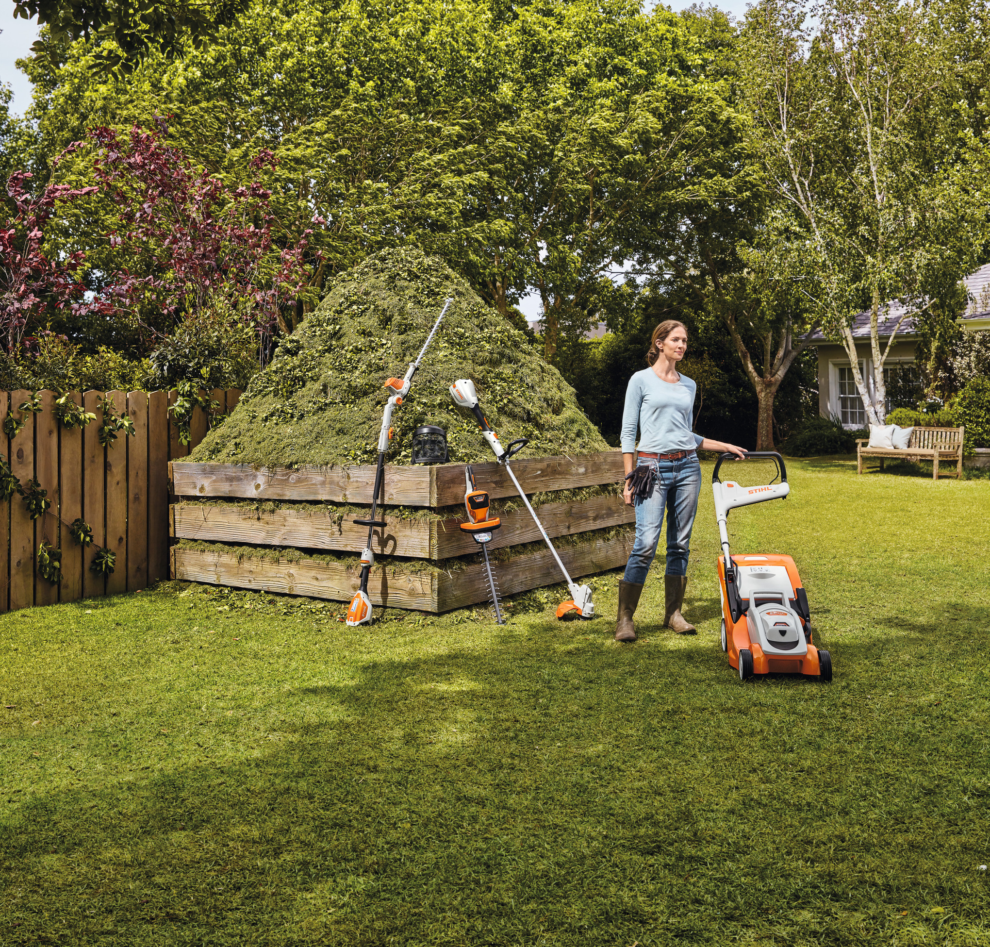 Une femme avec l'ensemble de ses outils STIHL devant un monticule de gazon coupé
